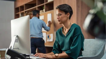 Woman typing at a desktop with a colleague in the background