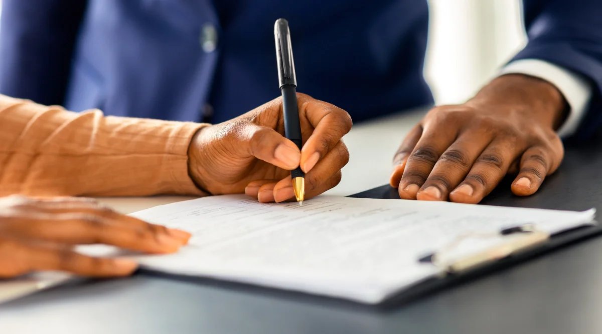 Close up on a hand signing a loan agreement in a formal office setting.